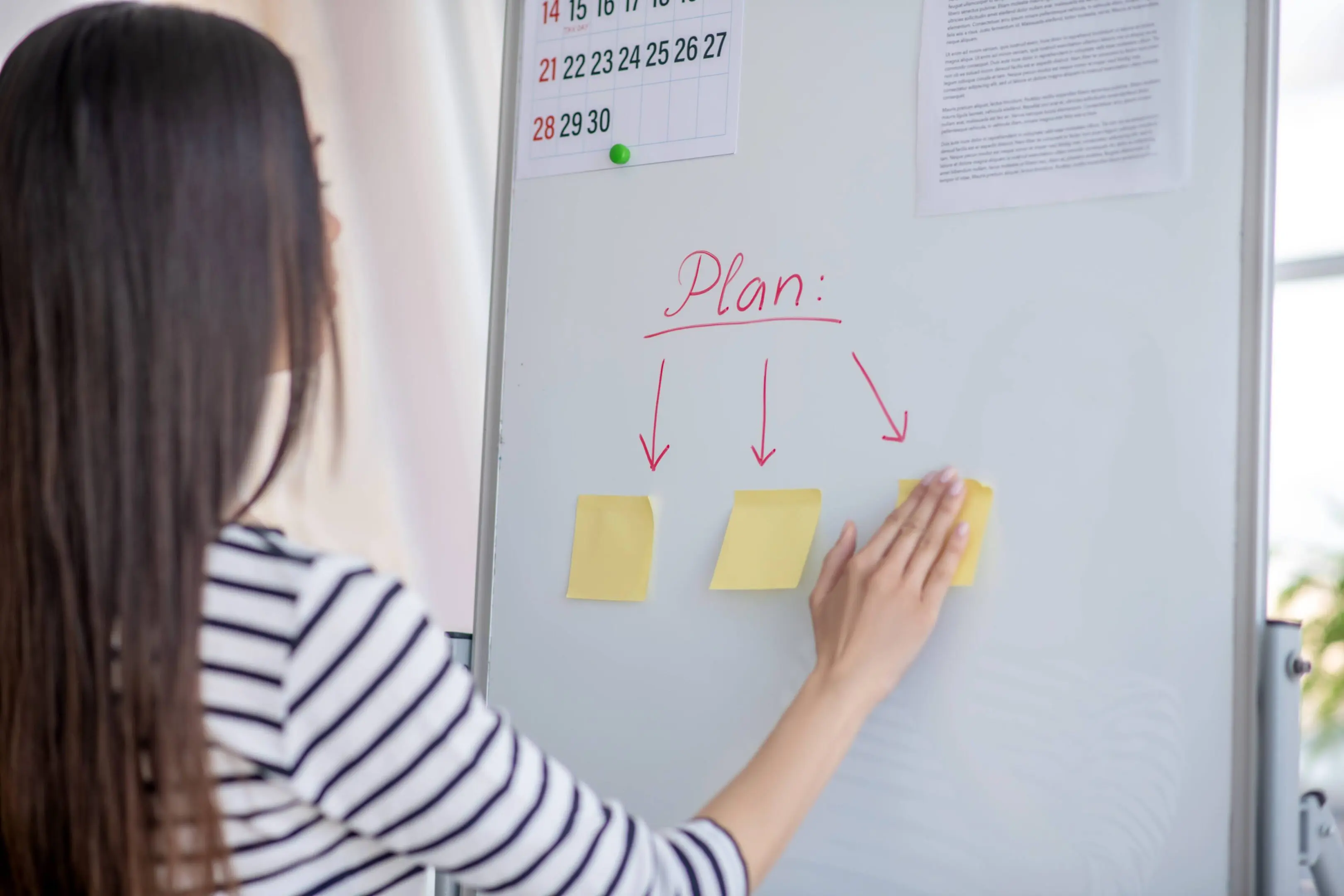 Woman organizing sticky notes on whiteboard.