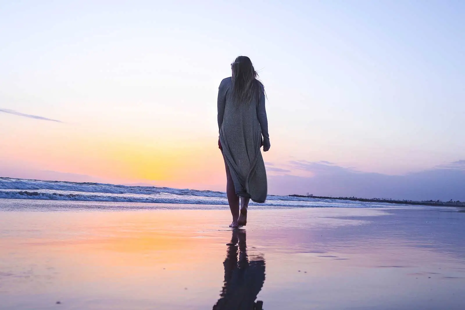 Woman walking on beach at sunset.