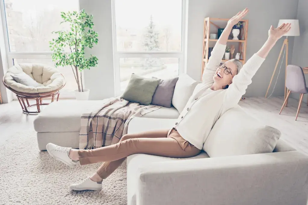 Elderly woman joyfully stretching on sofa.