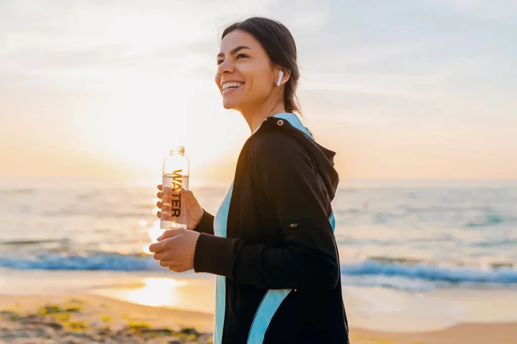 Woman jogging on beach with water bottle.